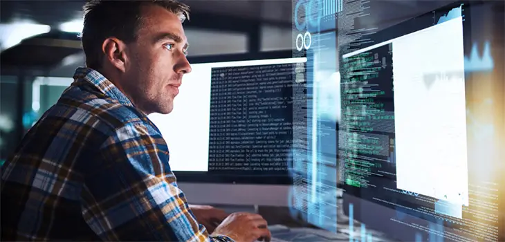 Male IT worker looking at computer screens with code on them.